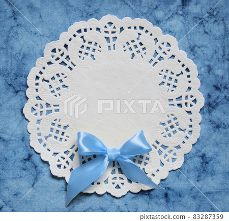 White round decorative napkin and satin bow on blue paper White round decorative napkin and satin bow on blue paper 83287359