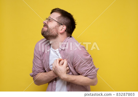 Caucasian bearded man is experiencing severe pain in the heart, holding his chest with his hands 83287803