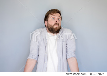 Bewilderment bearded man in a shirt shrugs in surprise and looks at the camera with a strange and 83287824