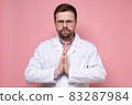 Serious, confident doctor in a white coat folded hands in supplication, palms together and calmly 83287984