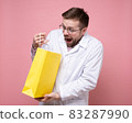 Young doctor received a gift, he holds a yellow package in hands, looks into it happily and is 83287990
