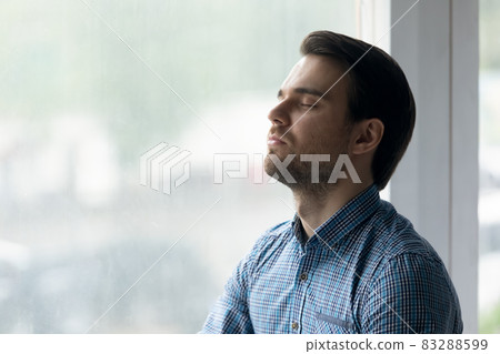 Close up mindful man with closed eyes meditating near window 83288599