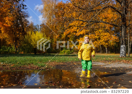 smiling child boy in yellow raincoat have fun with puddle smiling child boy in yellow raincoat have fun with puddle 83297220