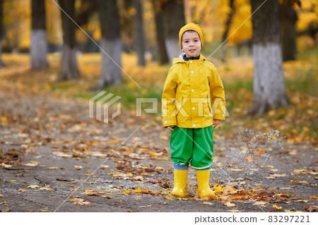 little boy with yellow raincoat walks in puddles 83297221