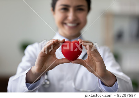 Smiling female cardiologist holding red heart, showing object at camera 83297687