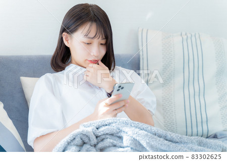 A woman looking at her smartphone with her thumb on her mouth 83302625