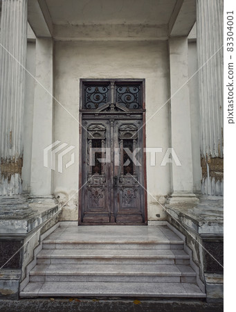 Vintage door and ornate facade details of an old historical building. Outdoors architecture elements, white columns on the doorsteps. Rustic wooden gate. The main entrance doorway Vintage door and ornate facade details of an old historical building. Outdoors architecture elements, white columns on the doorsteps. Rustic wooden gate. The main entrance doorway 83304001
