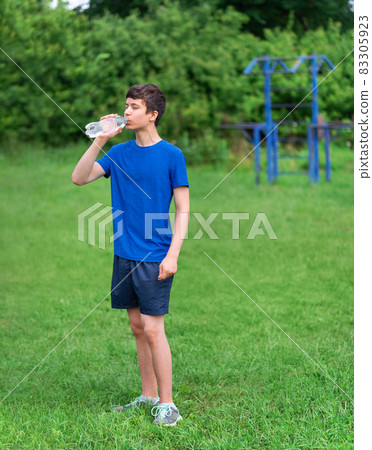 teenage boy exercising outdoors, sports ground in the yard, he opens a bottle of water and drinks, healthy lifestyle teenage boy exercising outdoors, sports ground in the yard, he opens a bottle of water and drinks, healthy lifestyle 83305923
