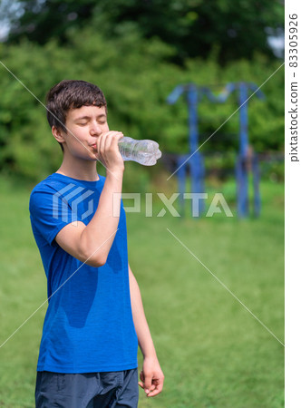 teenage boy exercising outdoors, sports ground in the yard, he opens a bottle of water and drinks, healthy lifestyle teenage boy exercising outdoors, sports ground in the yard, he opens a bottle of water and drinks, healthy lifestyle 83305926