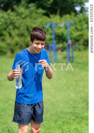 teenage boy exercising outdoors, sports ground in the yard, he opens a bottle of water and drinks, healthy lifestyle teenage boy exercising outdoors, sports ground in the yard, he opens a bottle of water and drinks, healthy lifestyle 83305928