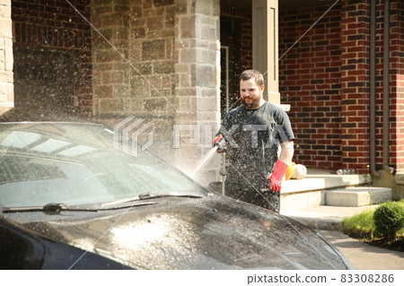 Caucasian man washing car by water and jet in front of house. Caucasian man washing car by water and jet in front of house. 83308286