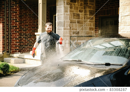 Man washing car by water and jet in front of house. Man washing car by water and jet in front of house. 83308287