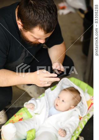 Young father taking photo by smartphone of little baby girl lying in bed. Young father taking photo by smartphone of little baby girl lying in bed. 83308288