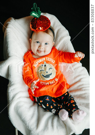 Baby in a Halloween pumpkin costume sitting on baby rocking chair smiling Baby in a Halloween pumpkin costume sitting on baby rocking chair smiling 83308837
