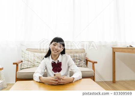 坐在沙發前,用智能手機聽音樂的高中女生 坐在沙發前,用智能手機聽音樂的高中女生 83309569