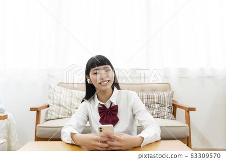 坐在沙發前,用智能手機聽音樂的高中女生 坐在沙發前,用智能手機聽音樂的高中女生 83309570