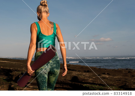 beautiful girl walking on the beach with yoga mat 83314918