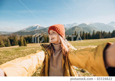 Young woman making selfie photo high in the snow mountains enjoying the view. Freedom, happiness, travel and vacations concept, outdoor activities, she wearing red hat and a yellow jacket Young woman making selfie photo high in the snow mountains enjoying the view. Freedom, happiness, travel and vacations concept, outdoor activities, she wearing red hat and a yellow jacket 83316622