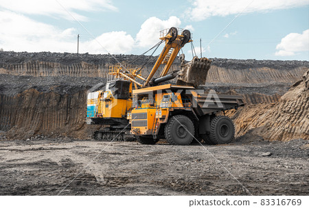 Large quarry dump truck. Big yellow mining truck at work site. Loading coal into body truck. Production useful minerals. Mining truck mining machinery to transport coal from open-pit production 83316769
