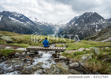 Man hiker resting on small bridge over mountaian river at Schlegeis Lake, Zillertal Alps, Austria 83317565