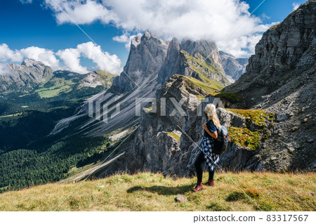 Adult women with backpack enjoy landscape of Seceda peak in Dolomites Alps, Odle mountain range, South Tyrol, Italy, Europe. Travel vacation concept Adult women with backpack enjoy landscape of Seceda peak in Dolomites Alps, Odle mountain range, South Tyrol, Italy, Europe. Travel vacation concept 83317567