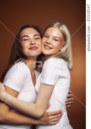 two pretty diverse girls happy posing together: blond and brunette, caucasian and asian on brown background, lifestyle people concept 83318547