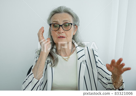 Tired senior grey haired businesswoman in striped jacket with eyeglasses is working in her office sitting at the desk and feeling bad due to menopause, menopause relief concept 83321006