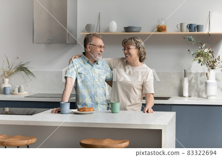 Bonding affectionate older couple talking in kitchen. Bonding affectionate older couple talking in kitchen. 83322694