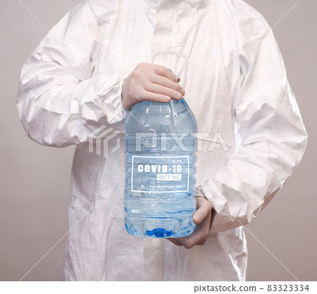 a man in a protective suit and gloves holds a large plastic bottle with the inscription covid 19 vaccine. the concept of permanent vaccination. close-up. 83323334