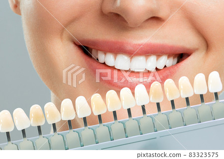 Smiling young woman. Cosmetological teeth whitening in a dental clinic. selection of the tone of the implant tooth 83323575