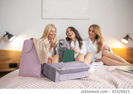 Laughing women on bed surrounded by shopping bags 83326825
