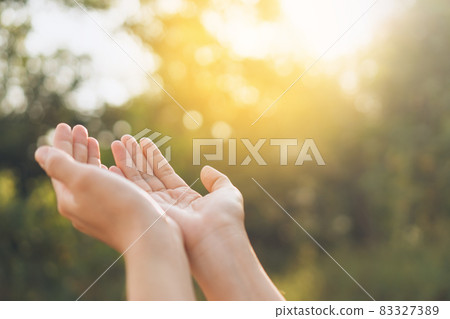 Woman open hand up to sunset sky and green blur leaf bokeh sun light abstract background. 83327389