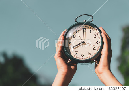 Woman raise hand up and holding clock on blue sky abstract background. 83327407