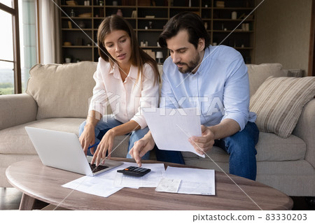 Concentrated young family couple calculating expenditures. Concentrated young family couple calculating expenditures. 83330203