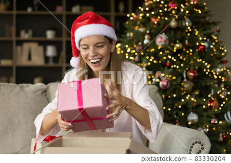 Happy excited Xmas girl in Santa hat unpacking received box Happy excited Xmas girl in Santa hat unpacking received box 83330204