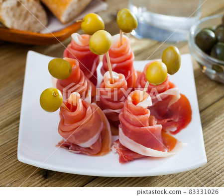 Spanish tasty meal rolls of iberian jamon served with olives at plate 83331026