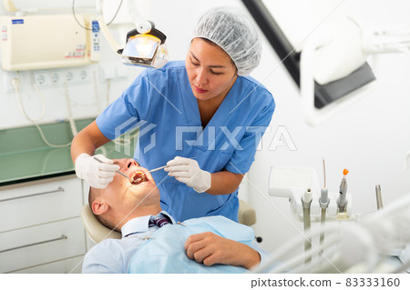 Dentist is treating male patient which is sitting in dental chair 83333160