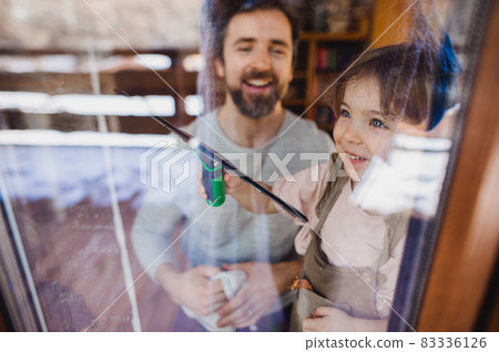 Happy girl with father cleaning windows at home, daily chores concept. Shot through glass. Happy girl with father cleaning windows at home, daily chores concept. Shot through glass. 83336126