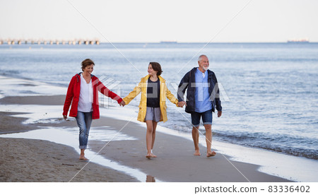 Senior couple holding hands with their preteen granddaughter and walking on sandy beach. Senior couple holding hands with their preteen granddaughter and walking on sandy beach. 83336402