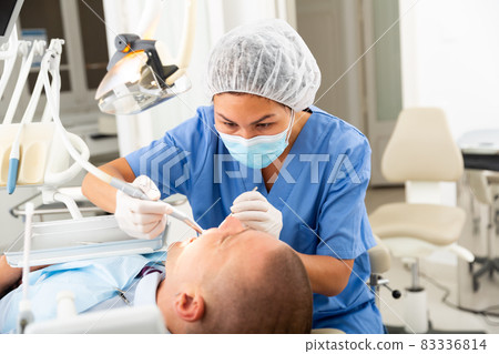 Female dentist drilling tooth to male patient Female dentist drilling tooth to male patient 83336814