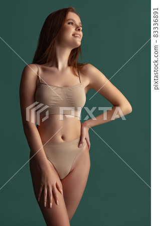 Cropped portrait of beautiful tender woman posing in beige underwear isolated over green background. Fitness Cropped portrait of beautiful tender woman posing in beige underwear isolated over green background. Fitness 83336891