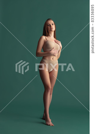Full-length portrait of beautiful tender woman posing in beige underwear isolated over green background Full-length portrait of beautiful tender woman posing in beige underwear isolated over green background 83336895