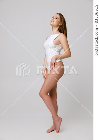 Full-length portrait of beautiful young woman in white bodysuit posing isolated over gray background Full-length portrait of beautiful young woman in white bodysuit posing isolated over gray background 83336915