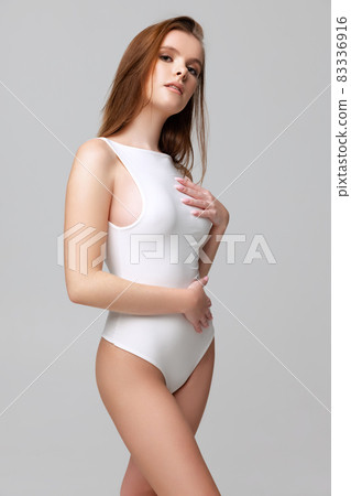 Cropped portrait of beautiful young woman in white bodysuit isolated over gray background 83336916