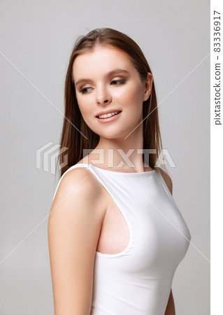 Cropped portrait of beautiful young woman with nude makeup in white bodysuit isolated over gray background Cropped portrait of beautiful young woman with nude makeup in white bodysuit isolated over gray background 83336917