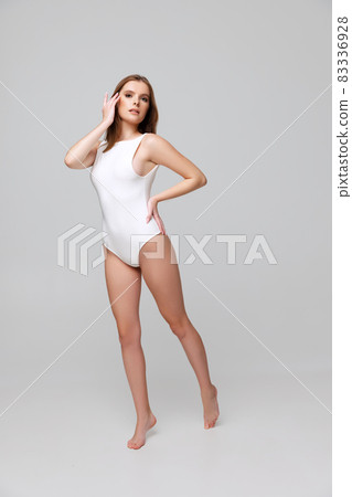 Full-length portrait of beautiful young woman in white bodysuit posing isolated over gray background Full-length portrait of beautiful young woman in white bodysuit posing isolated over gray background 83336928