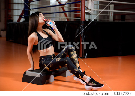 Attractive sports girl smiles and drinking water standing in fitness class. Attractive sports girl smiles and drinking water standing in fitness class. 83337722