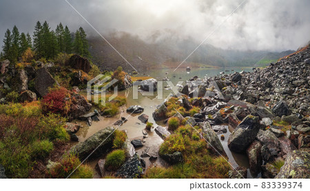 Panoramic view of the autumn mountain, fog over the mountain slopes in the distance, white clouds filling the mountain gorge. A clear blue mountain lake and a bright autumn forest. Panoramic view of the autumn mountain, fog over the mountain slopes in the distance, white clouds filling the mountain gorge. A clear blue mountain lake and a bright autumn forest. 83339374