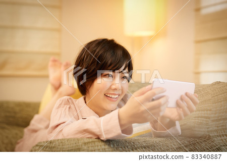 A young lady who lies on the sofa and watches a smartphone A young lady who lies on the sofa and watches a smartphone 83340887
