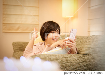 一位年輕的女士躺在沙發上，看著智能手機 83340888